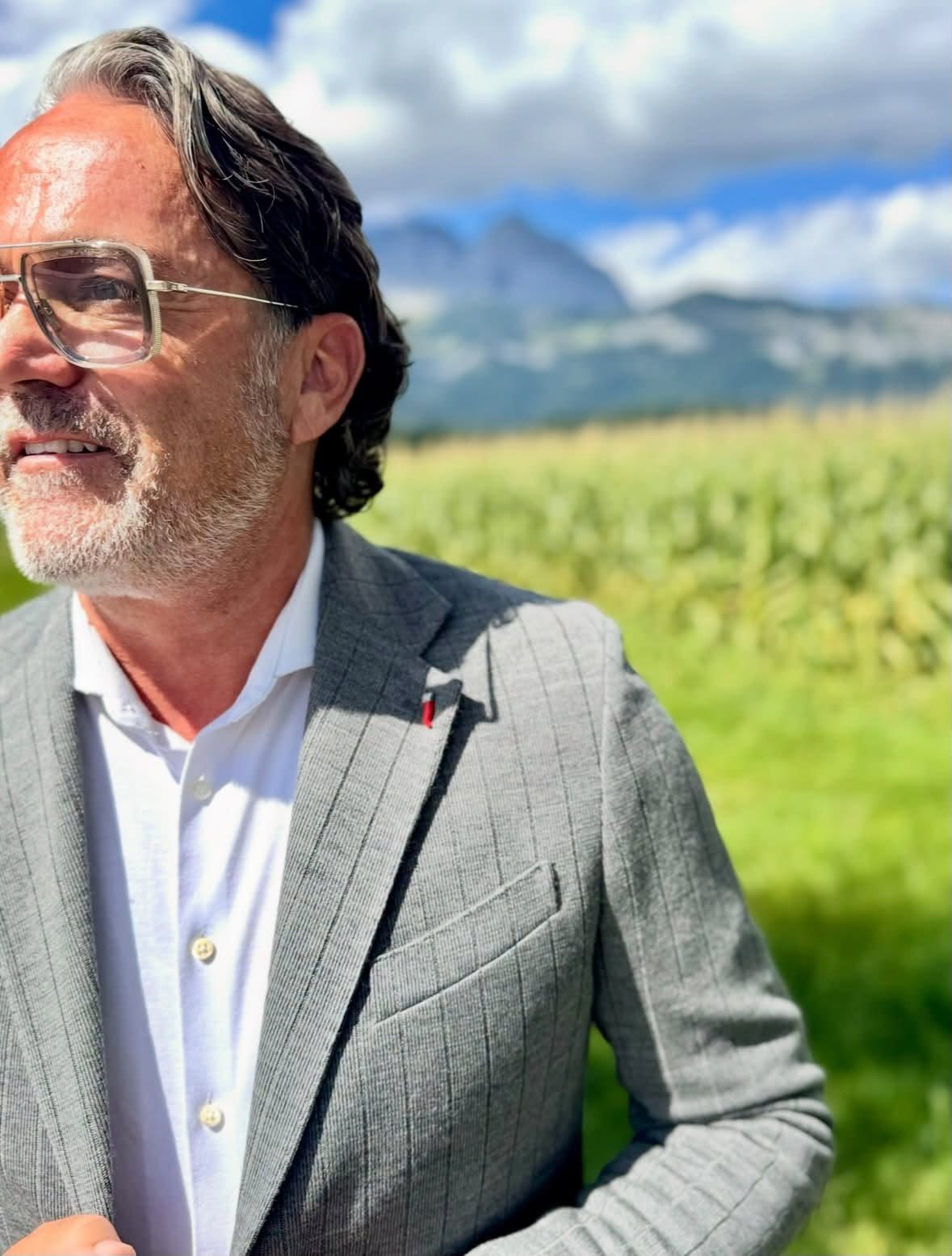 Alexander Desch im grauen Sakko vor Feldern und Bergen